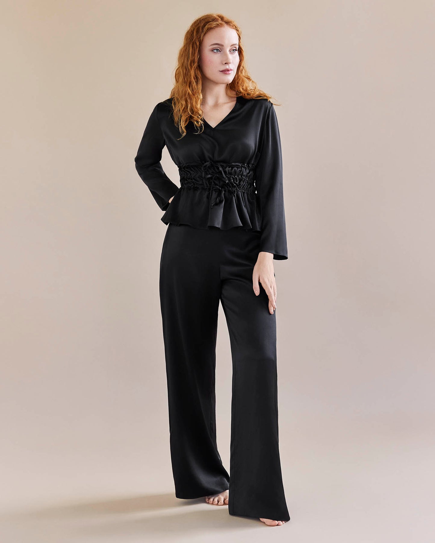Model wears black silk tie waist top coached in a waist for an hourglass look and a pair of black, silk, wide legged trousers with a tuxedo stripe
