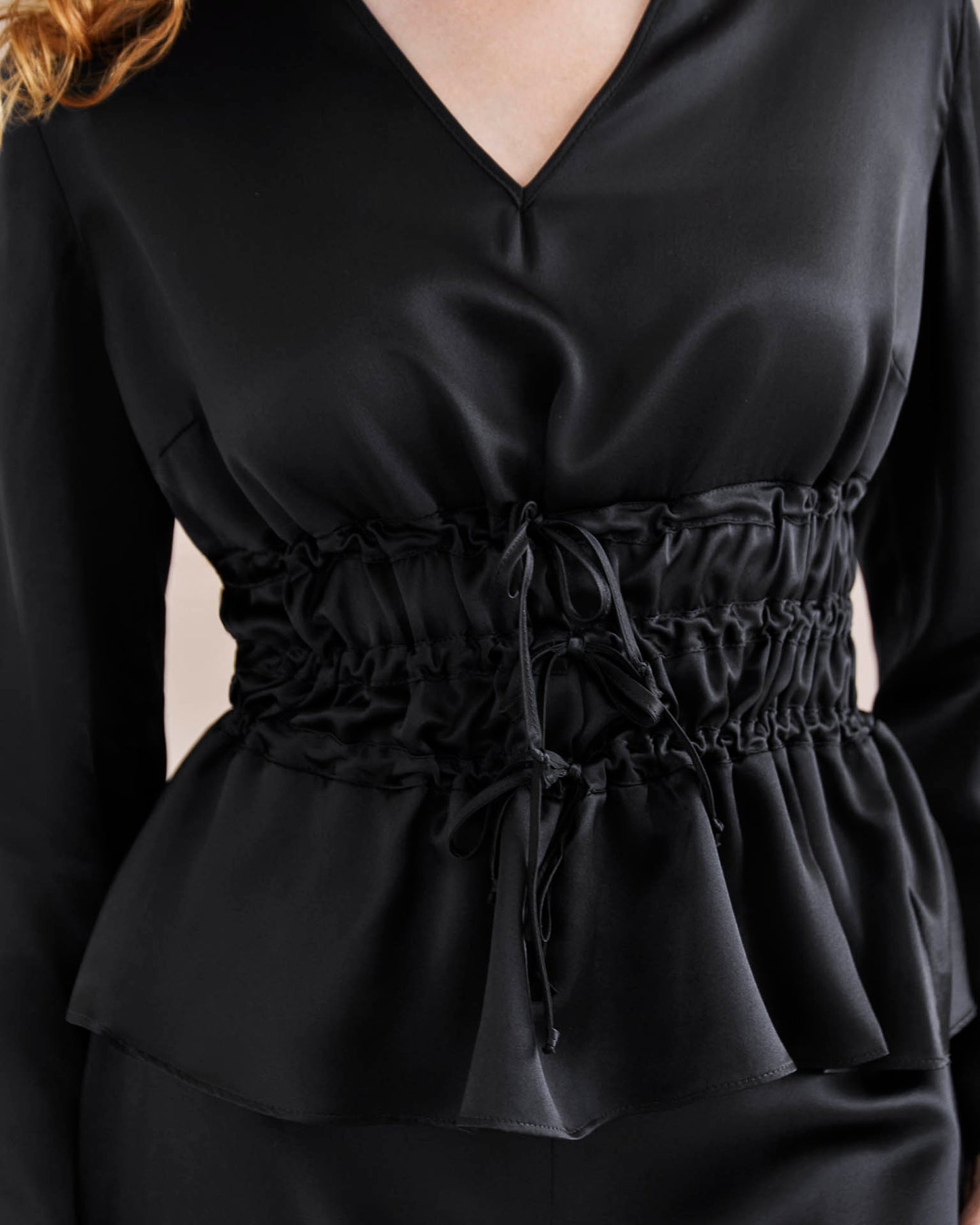 Detail shot. Model wears black silk tie waist top cinched in at the waist for an hourglass look.